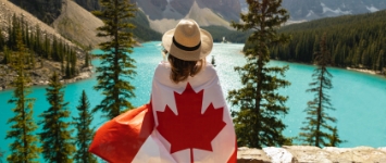 Uma mulher admirando uma vista de um lago, com uma bandeira do Canadá sobre suas costas