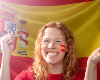 Uma mulher sorrindo tendo ao fundo uma bandeira da Espanha