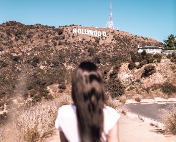 Mulher caminhando em direção a placa de Hollywood